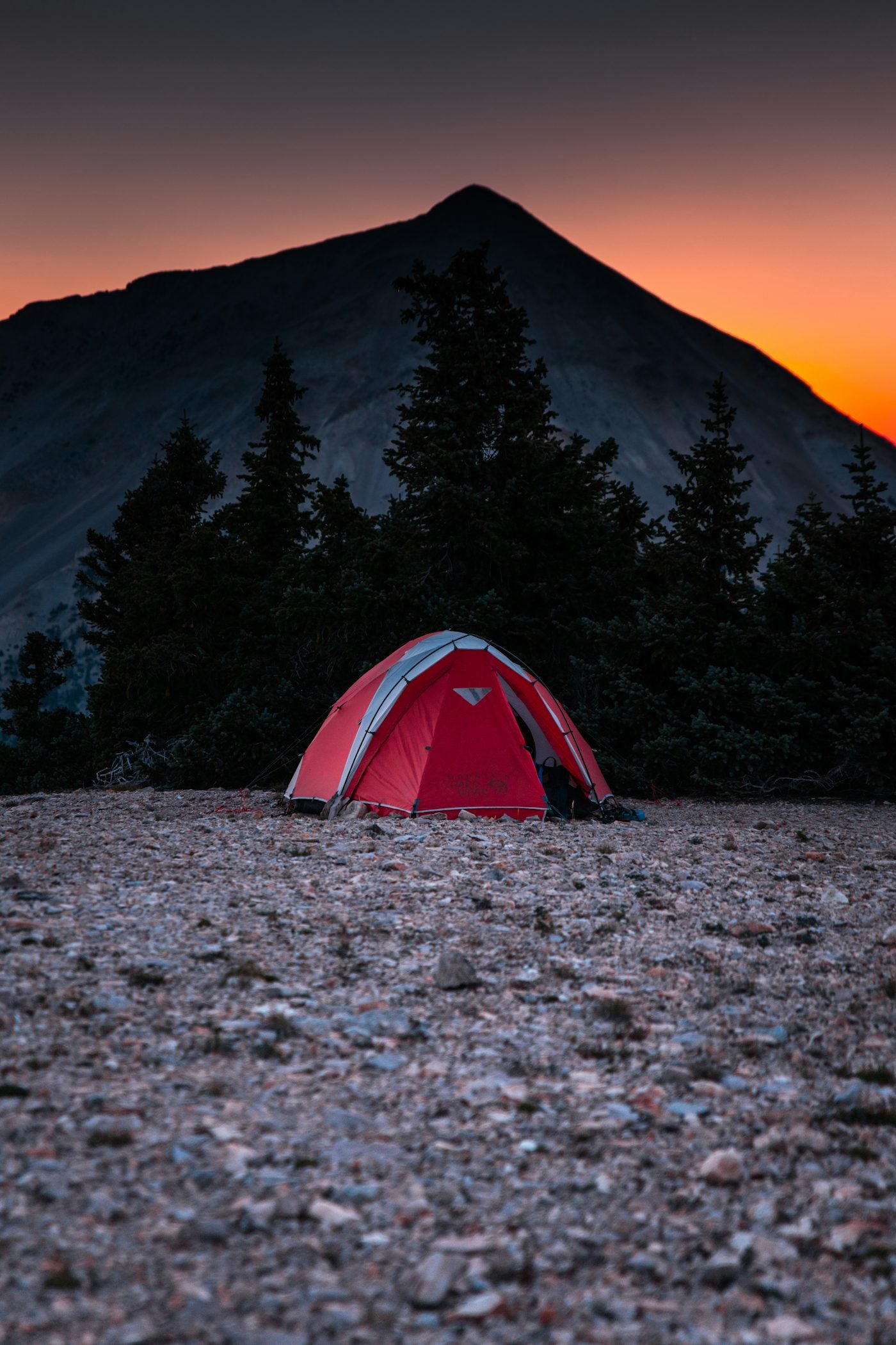 A tent glowing at dusk beneath a mountain peak